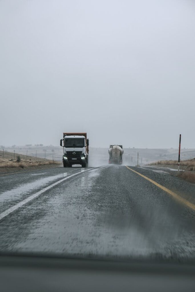 pexels-photo-29526703 Two trucks driving on a rainy highway with overcast skies and empty roadsides.